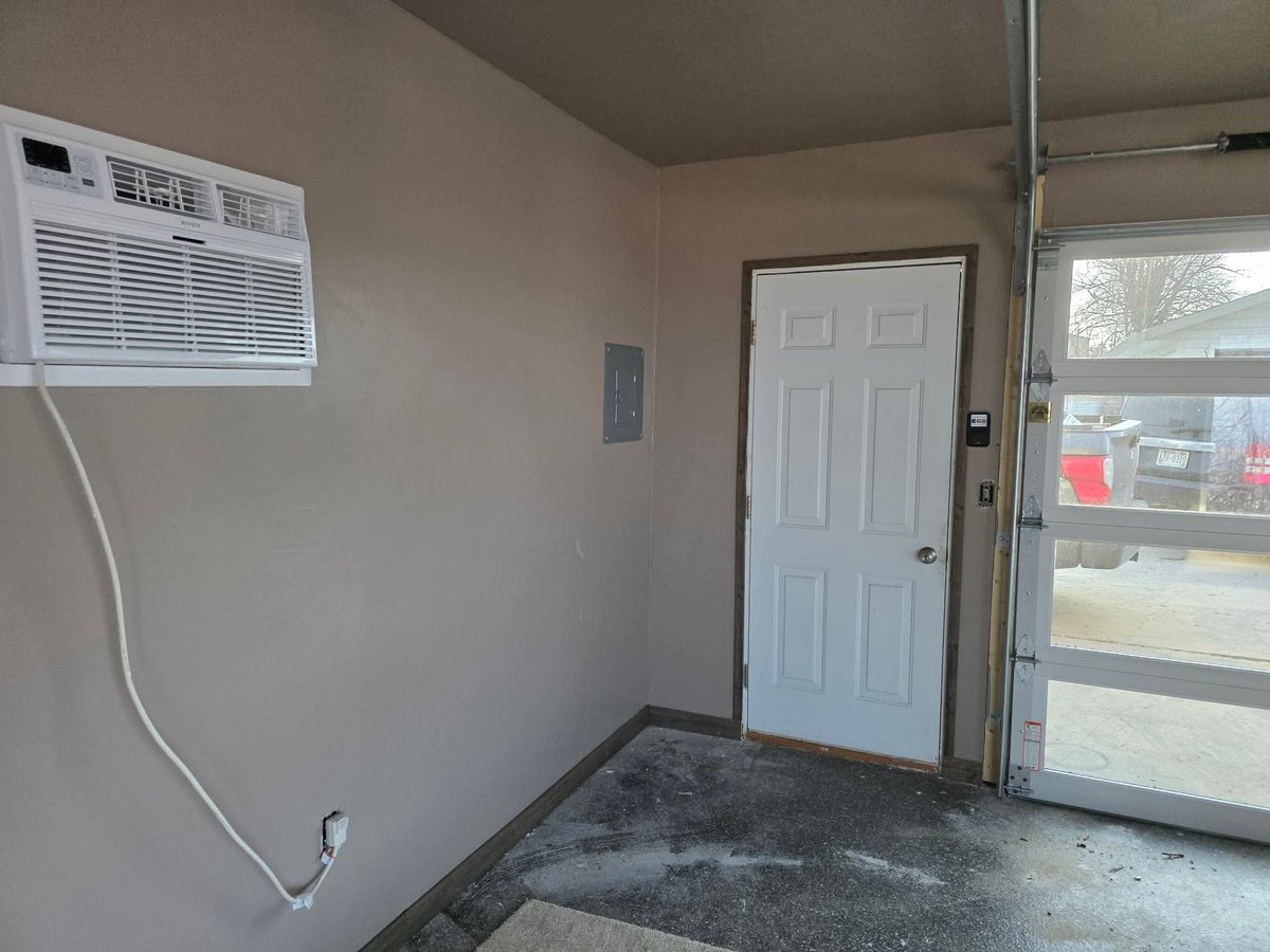 Empty room interior with window AC unit on wall, white door, glass sliding door with view outside, and concrete floor