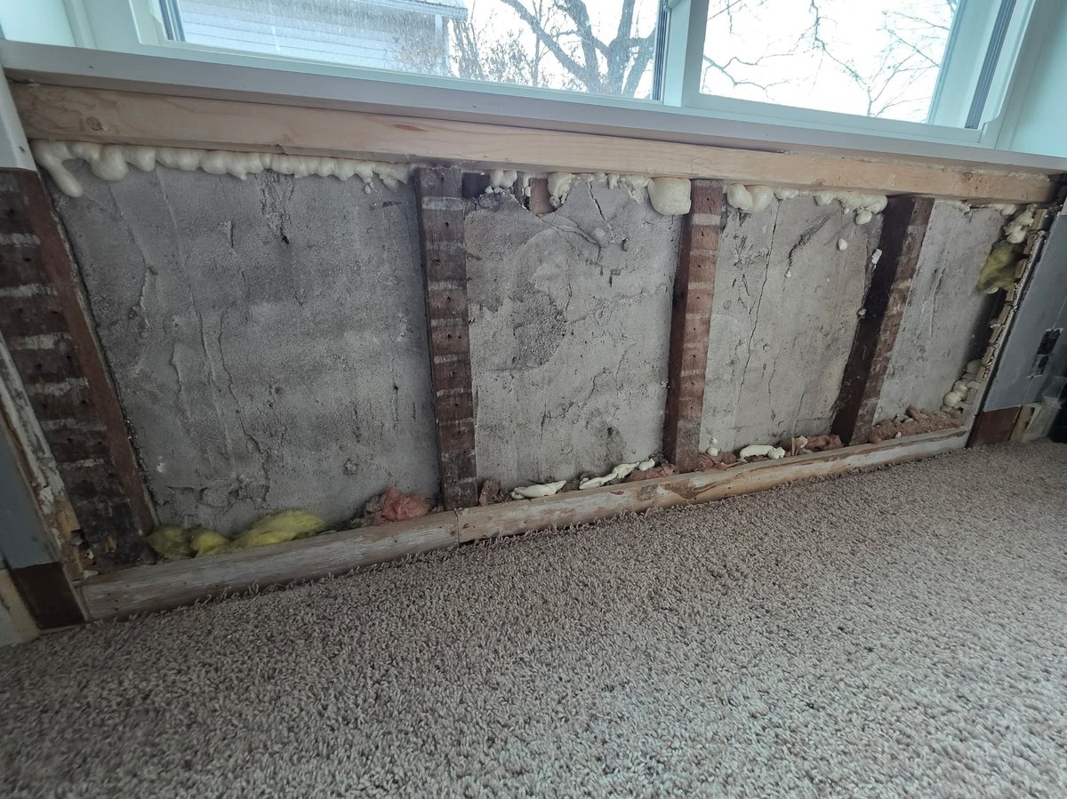 Weathered wooden panels with exposed brick columns in a frame against concrete floor and window background