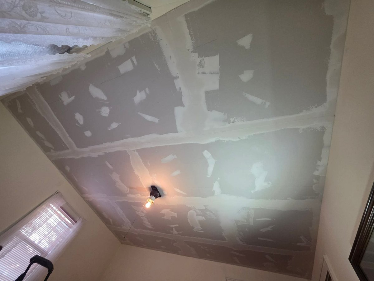 Construction or renovation ceiling with drywall sections, exposed framework, and plastic sheeting covering large openings