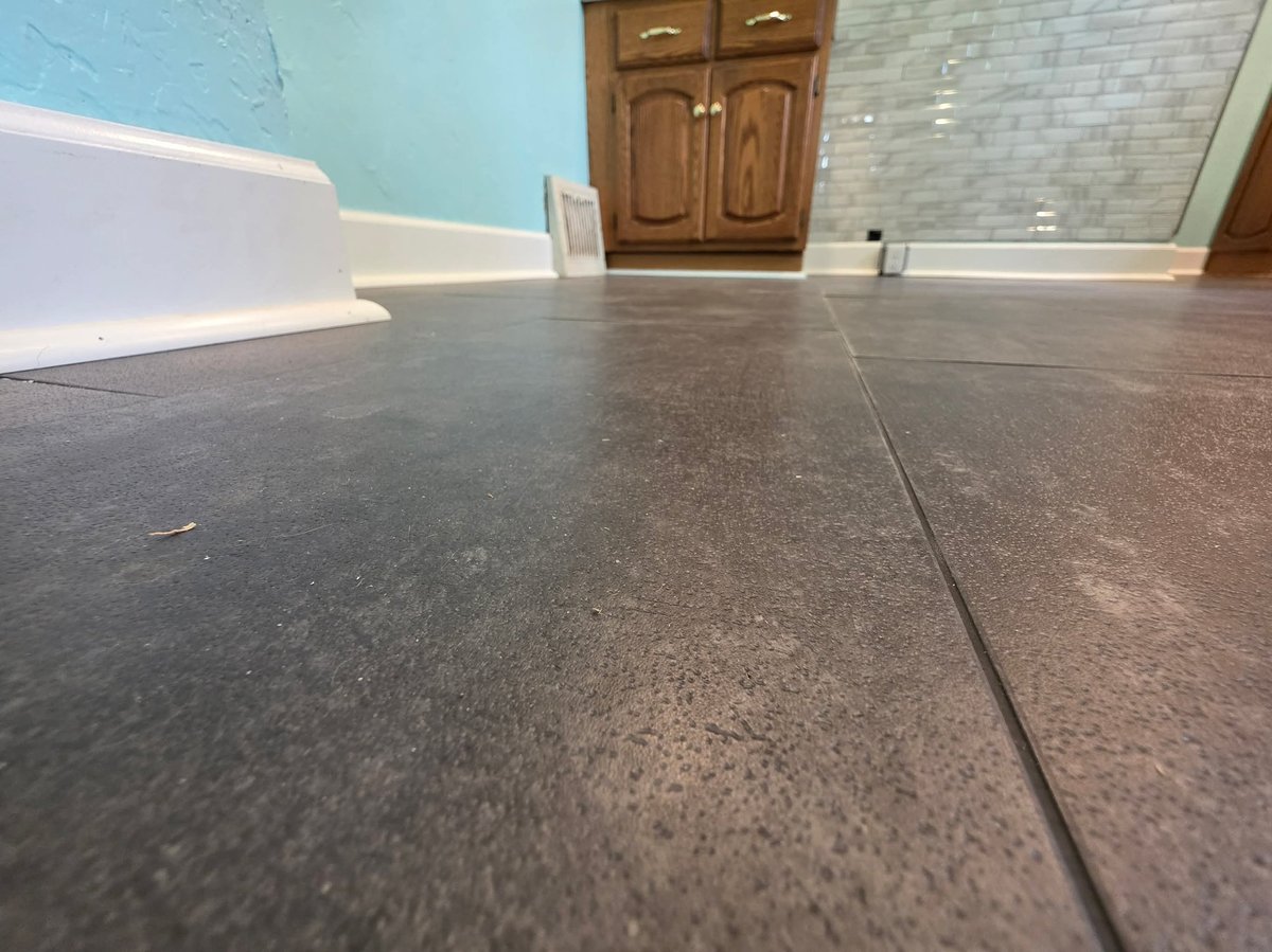 Low-angle view of a basement floor with visible seams, light blue walls, wooden cabinets, and white trim along the sides