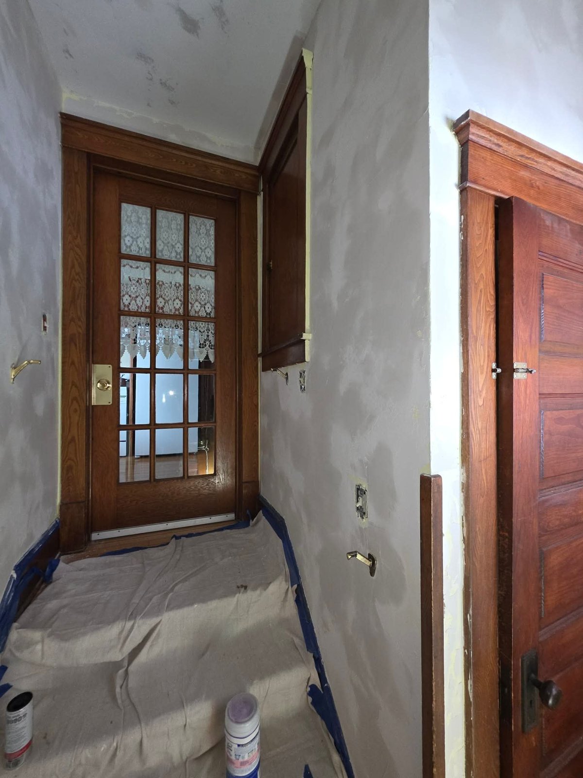 Construction hallway with wooden doors, white walls, plastic sheeting on floor, and drop cloths during interior renovation