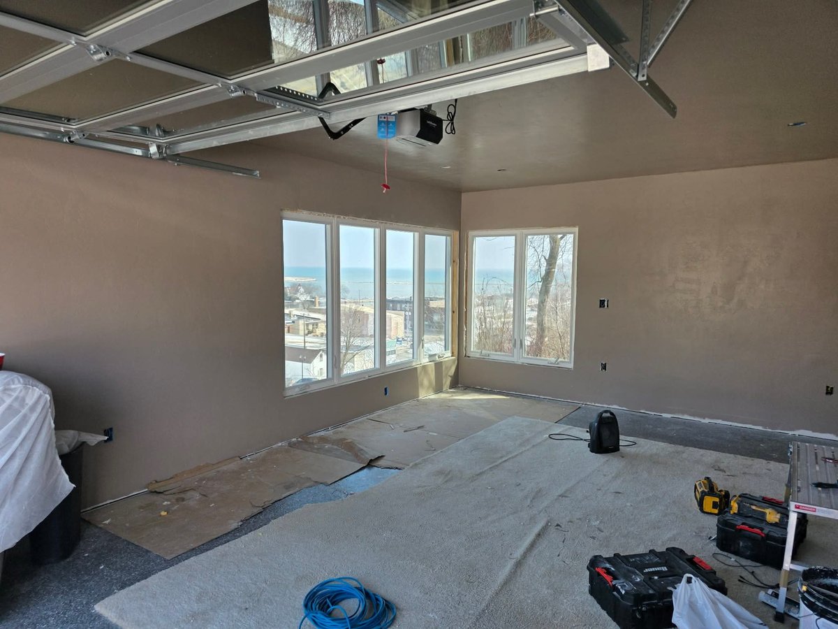 Unfinished interior room with drywall flooring, large windows overlooking cityscape, exposed ceiling with HVAC ducts and construction equipment