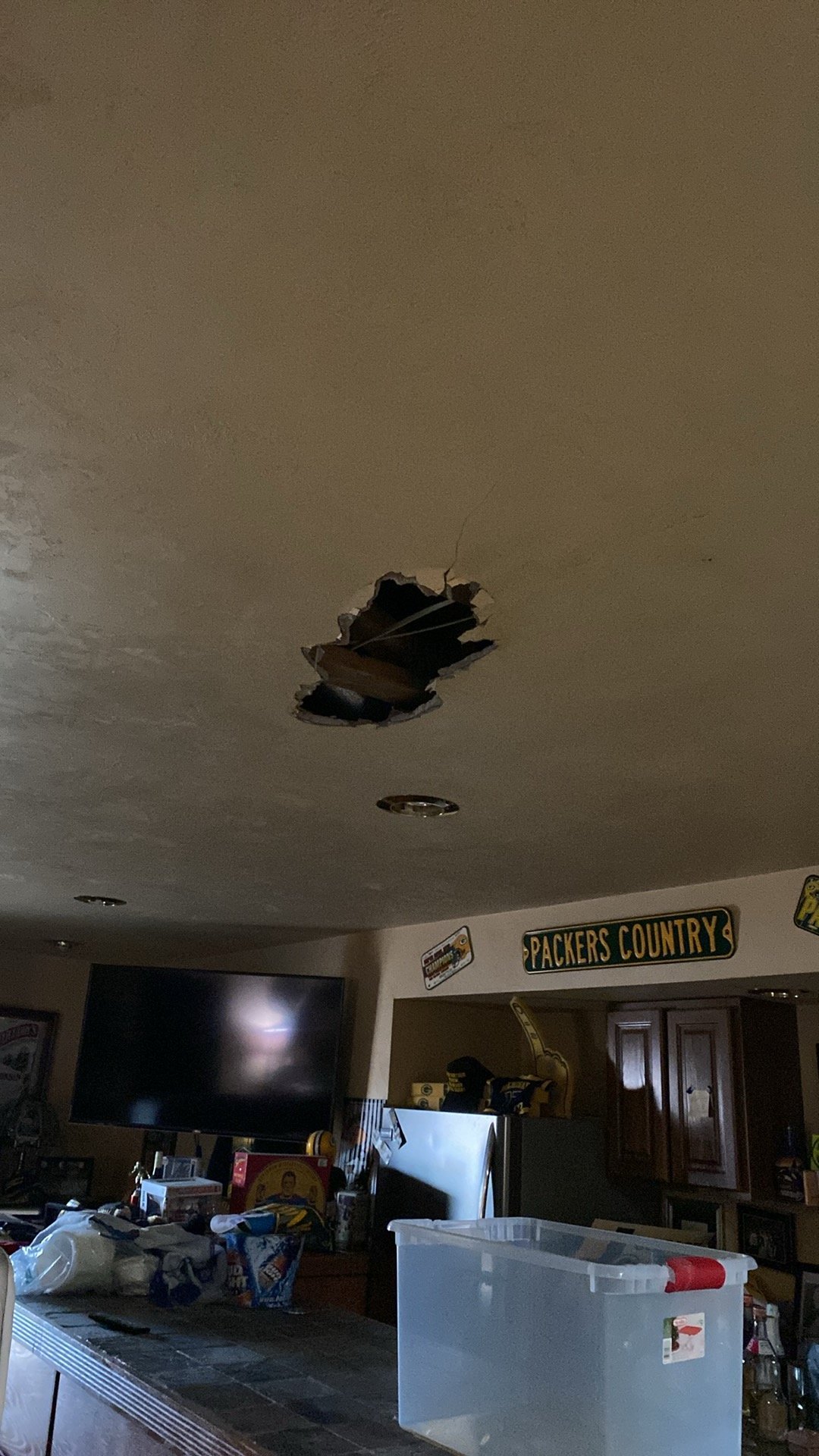 Damaged ceiling with torn drywall and dark debris hole in residential room with TV and furniture below