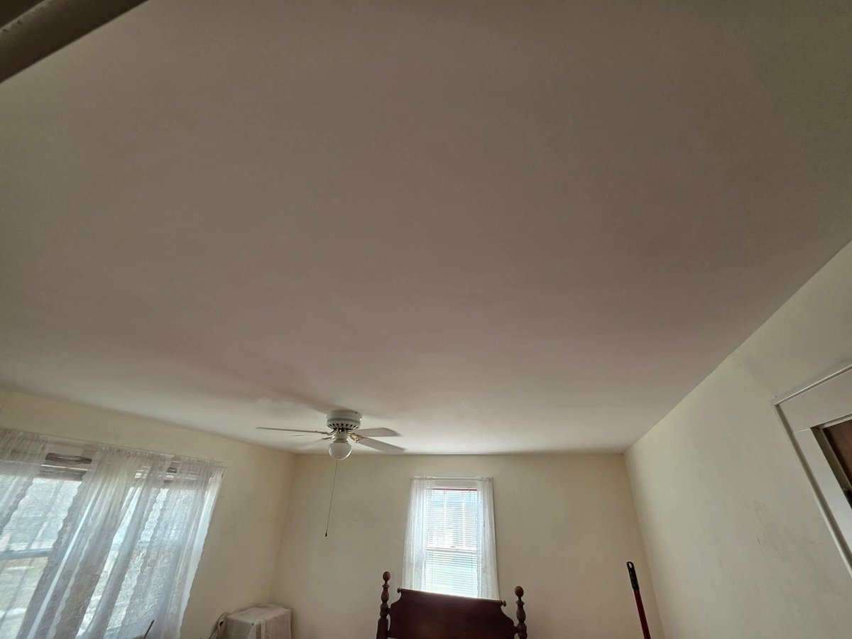Interior bedroom with ceiling fan, two windows with curtains, and bedframe visible