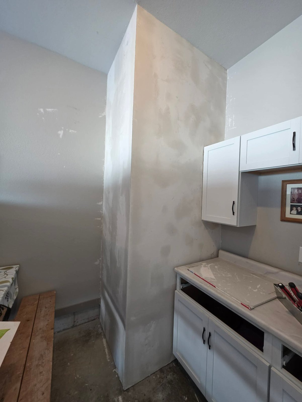 Large plastic-wrapped refrigerator in kitchen renovation with white cabinets and countertops visible to the right