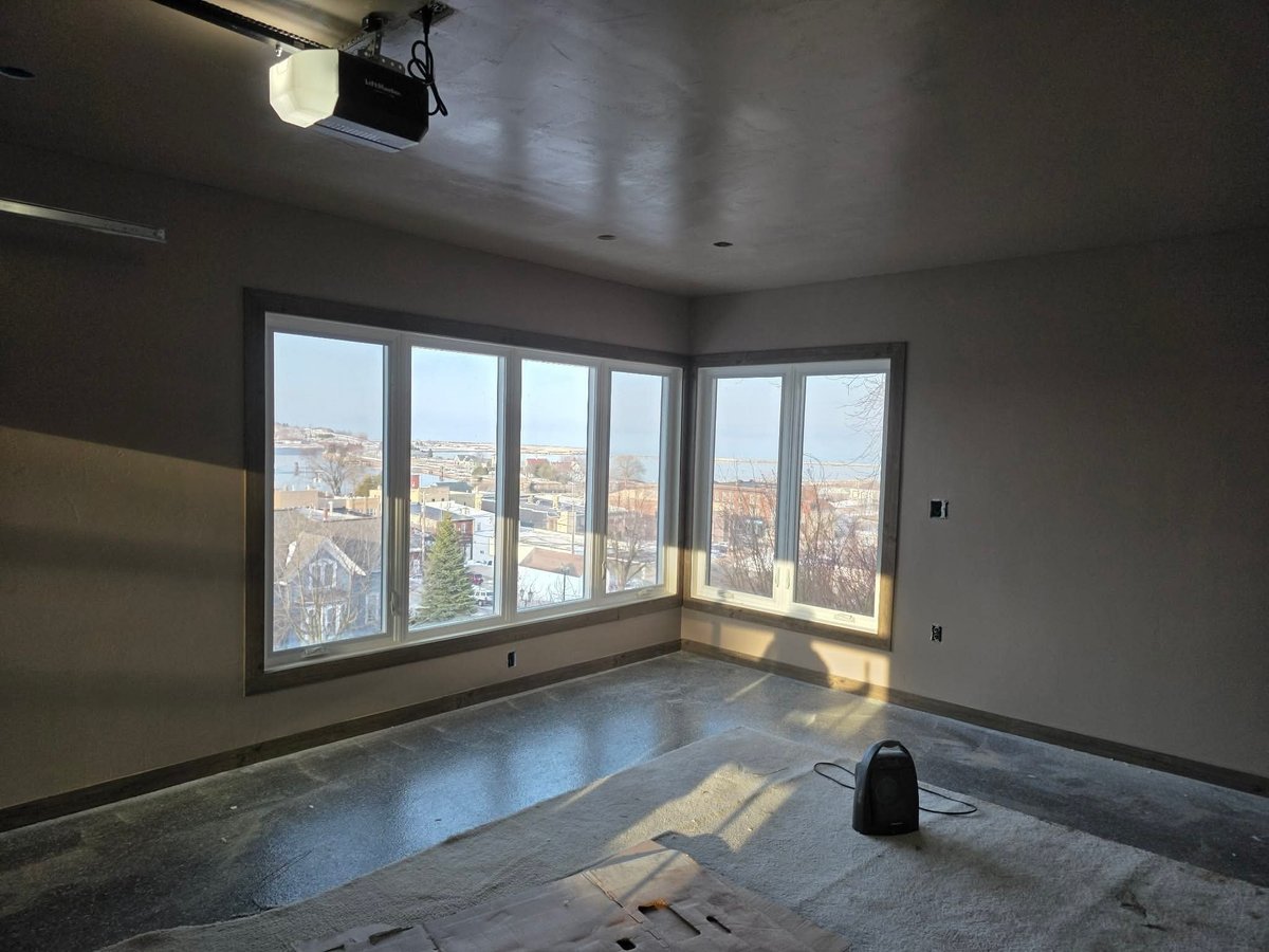 Empty modern room with large corner windows overlooking a city, concrete flooring, and a projector on the ceiling
