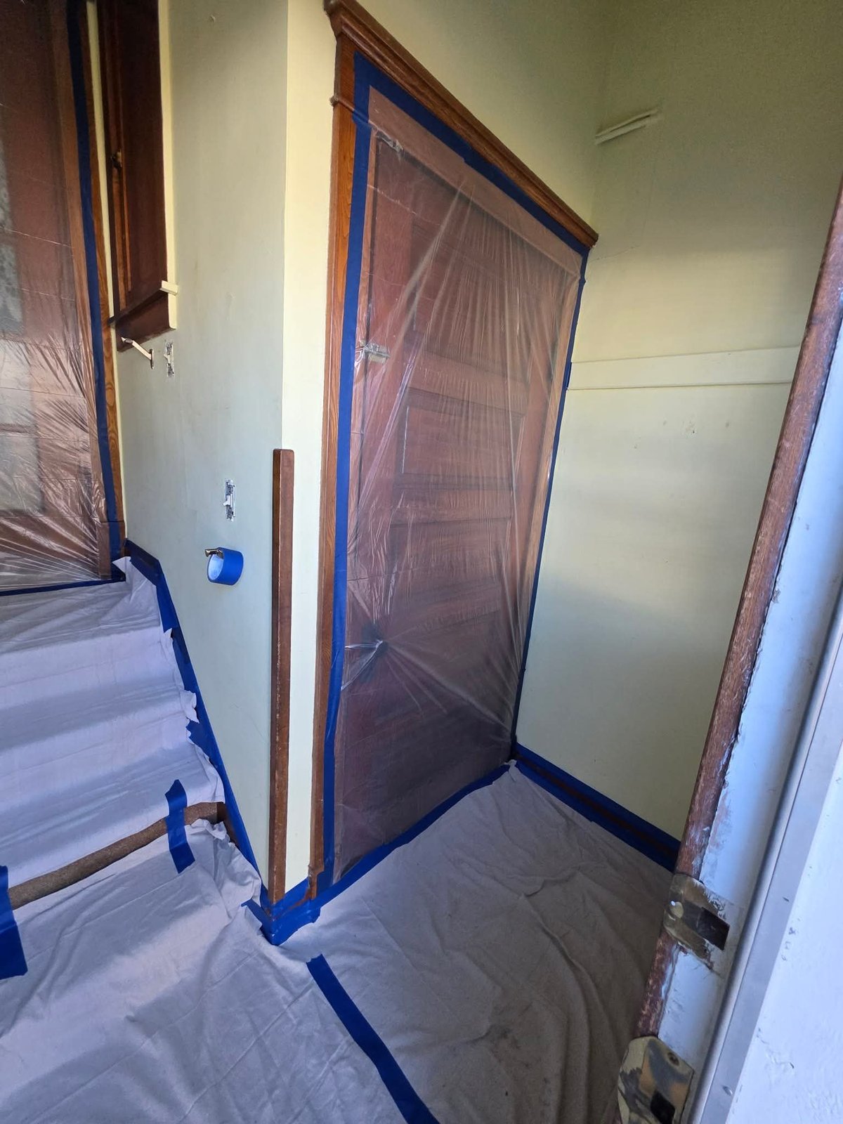 Construction room with protective plastic sheeting over doorways and blue painters tape outlining work areas