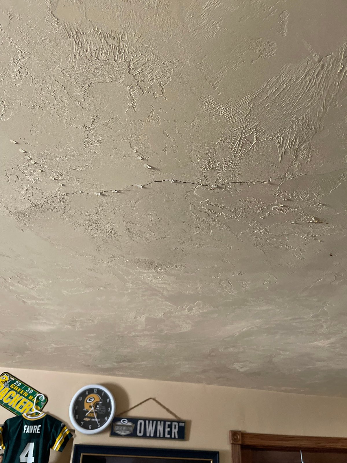 Damaged ceiling with cracks, water stains, and peeling texture paint above sports memorabilia on wall