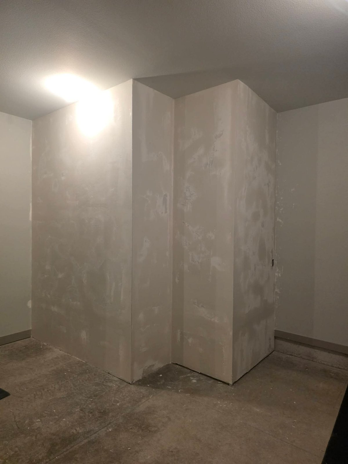 Drywall construction frame in an unfinished room with concrete floor and ceiling light fixture